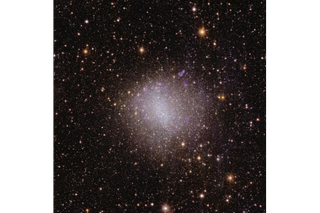 A sparkling pink and white patch of light in the center of the frame, surrounded by millions of spots of light representing distant cosmic objects.