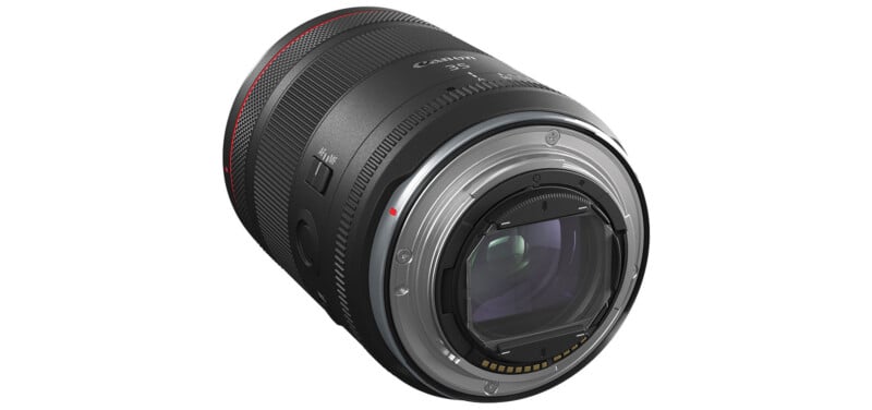 A close-up of a Canon camera lens.  The lens features various switches and markers and is largely black with a red accent ring at the end.  The inner glass elements and electronic contacts on the mounting side are visible.