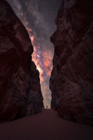 The Milky Way photographed between two high cliffs, with a lone man in the middle