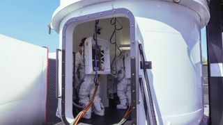 astronauts in white space suits stand in a white airlock