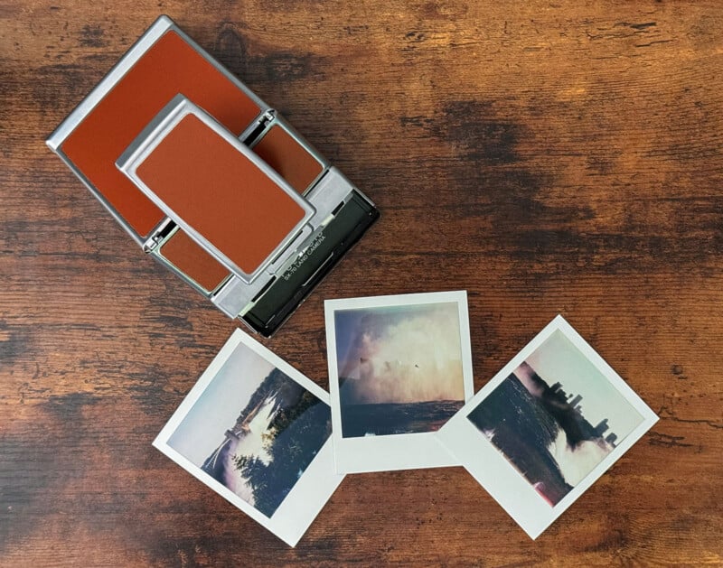 A vintage Polaroid camera with a brown and silver design sits on a wooden surface.  In front of the camera are three instant photos of outdoor scenes, including a forest, a body of water, and a cityscape with cloudy skies.