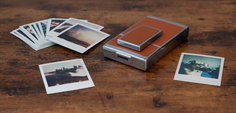 A collection of instant photos spread across a wooden surface.  A dog can be seen in one photo on the right.  In the center is a vintage instant camera with a brown leather cover.  More photos are partially visible in two stacks on the left side of the camera.