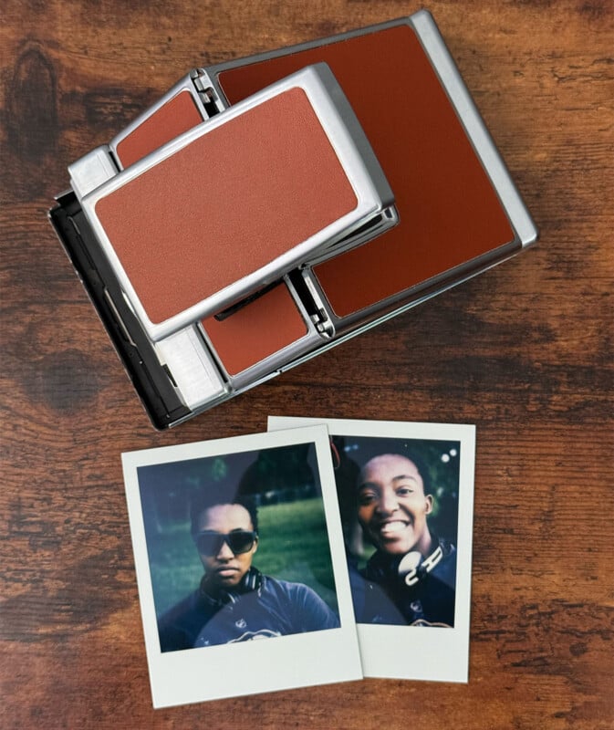 A vintage Polaroid camera with a brown and silver design on a wooden surface, accompanied by two instant film photos.  The photos show two smiling people, each wearing sunglasses and headphones.