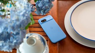 The blue Google Pixel 8a on a tea leaf with blue hydrangeas above it