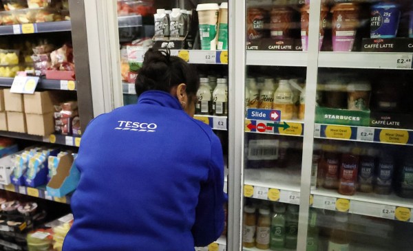 A Tesco employee stocking the refrigerator shelves 