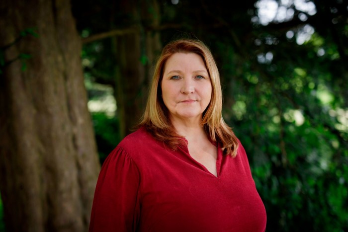 A woman in a red blouse stands under a large tree