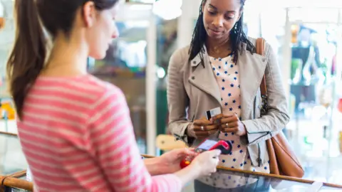 Getty Images A woman about to buy something in a store using a debit or credit card