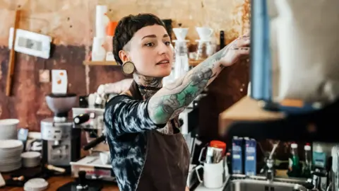 Getty Images A woman with tattooed arms and neck working in a coffee shop