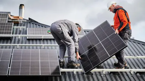 Getty Images Two men are attaching solar panels to a roof