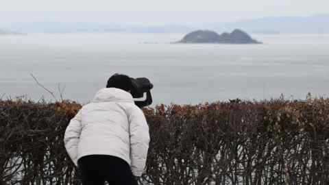 A man looks through binoculars at the North Korean coastline from a viewpoint in South Korea