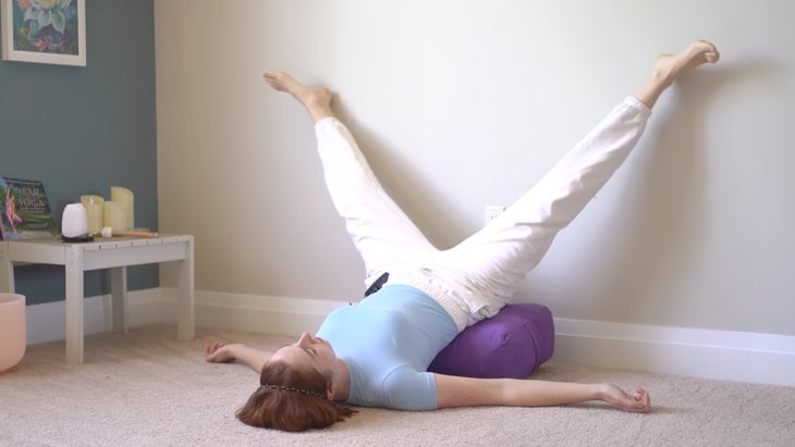 woman practicing yoga against a wall with her feet in a narrow crevice