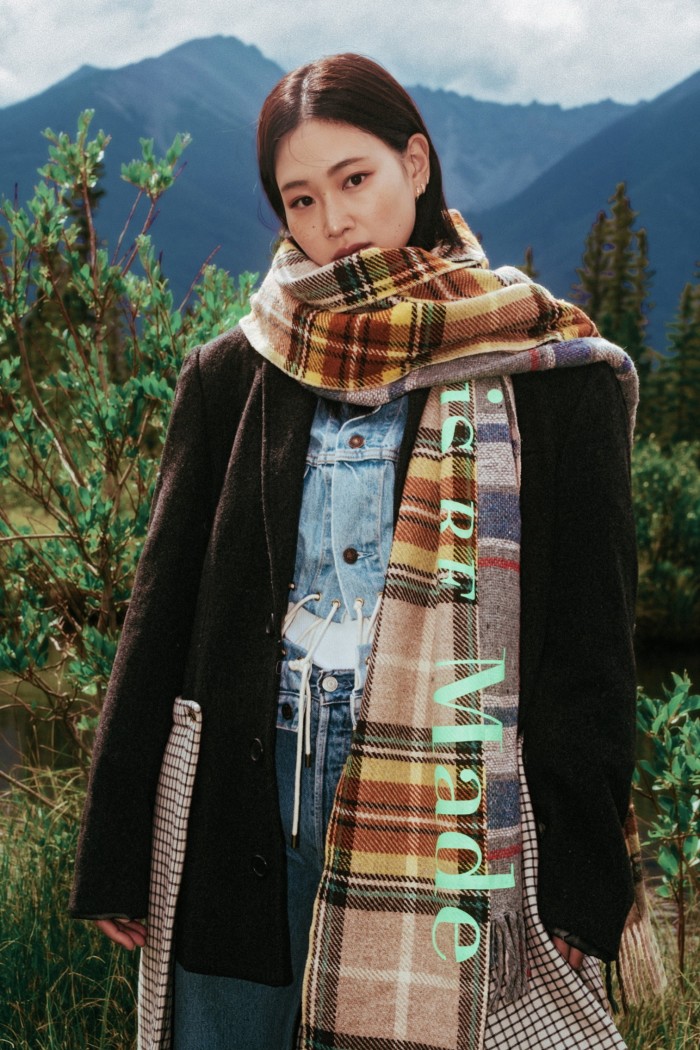 A woman in the countryside wears a checked scarf and a dark jacket