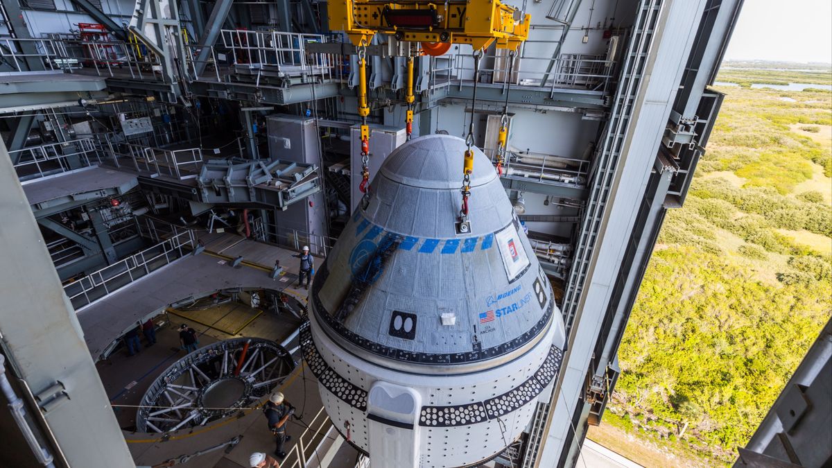 a cone-shaped spacecraft inside a tall facility with an open door to the right, showing trees and swamp down below