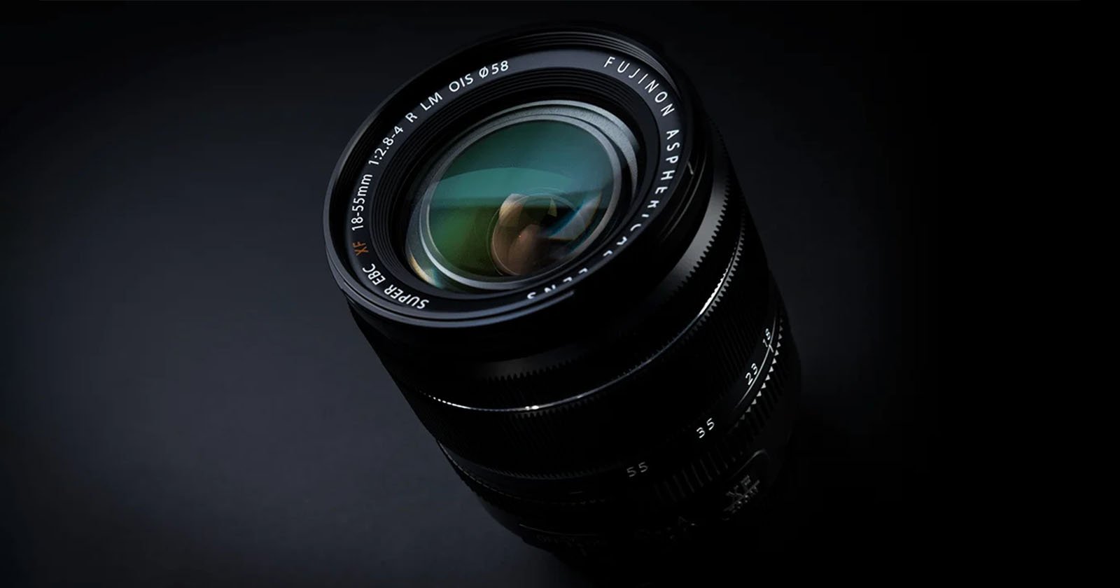 Close-up shot of a Fujinon camera lens against a black background. The lens has reflections visible on its glass, with the text "Fujinon Aspherical Super EBC" and the specifications "18-55mm 1:2.8-4 R LM OIS" around the outer edge.