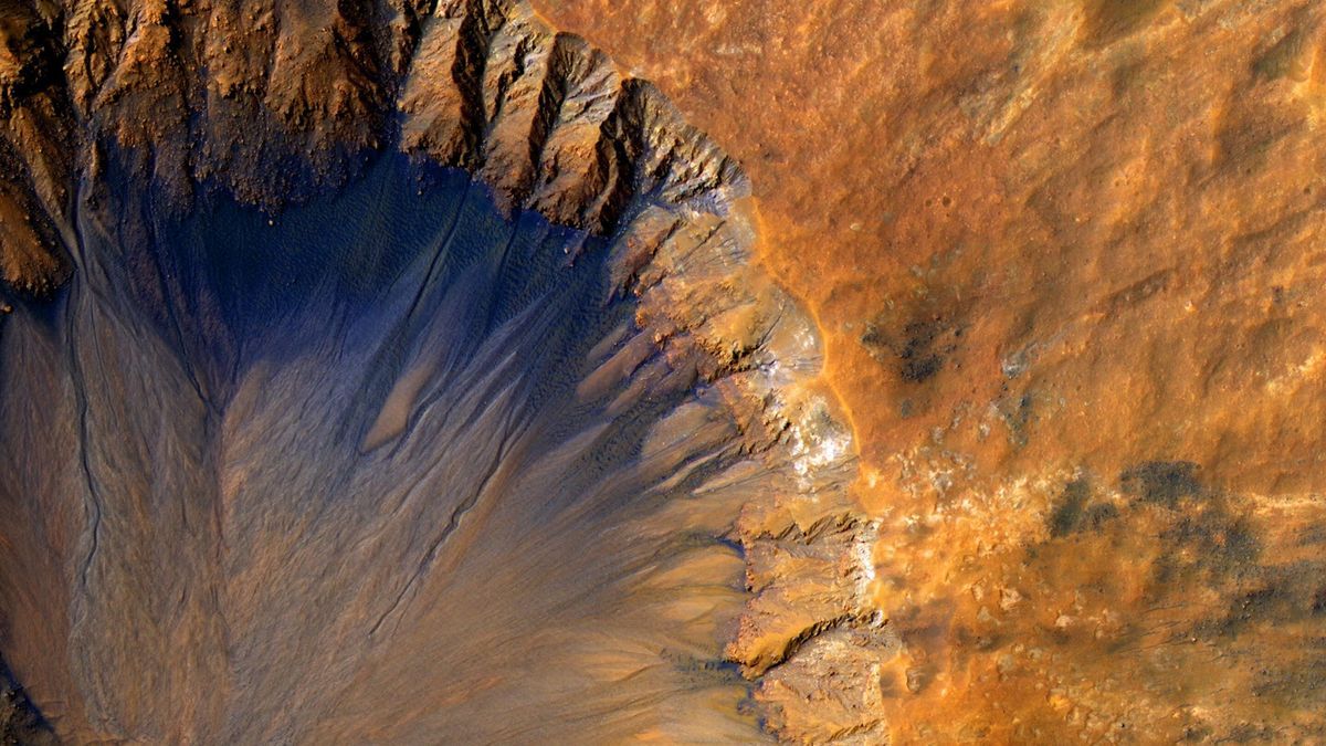 a deep, dark crater stands out on a reddish-orange planet