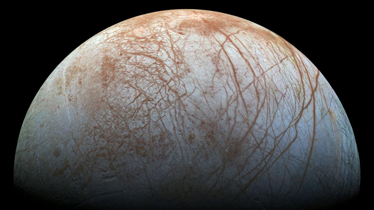 closeup of an icy moon, whose white surface is crisscrossed by reddish-brown lines