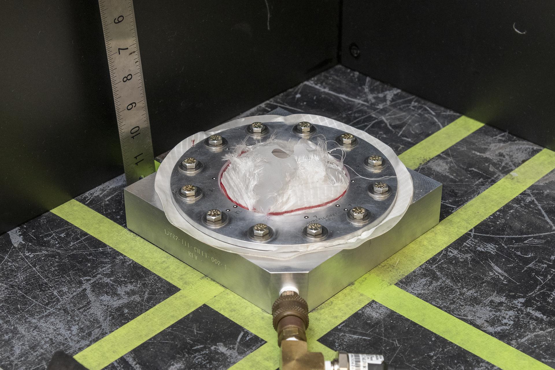 Fabric in a round test fixture fails after pressure is applied.