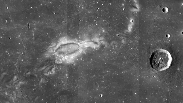 A dark grey high altitude view of the lunar surface, with tiny craters speckled throughout, and one large crater on the far right.